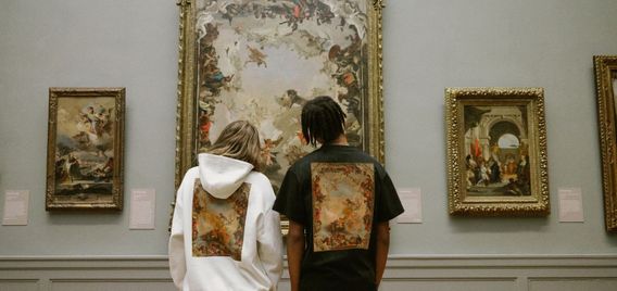 Two people stand in front of paintings at a museum.